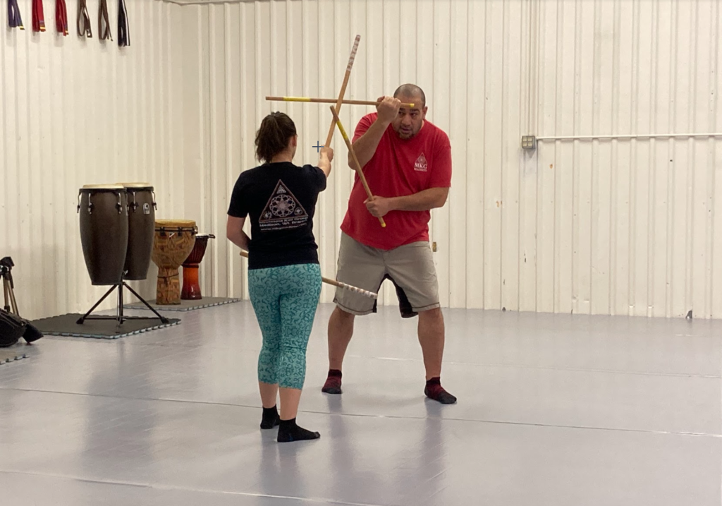 A man teaches a woman a technique with escrima sticks.