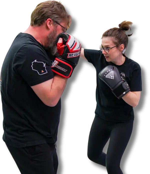 Woman throwing punch at trainer holding pads in Muay Thai class