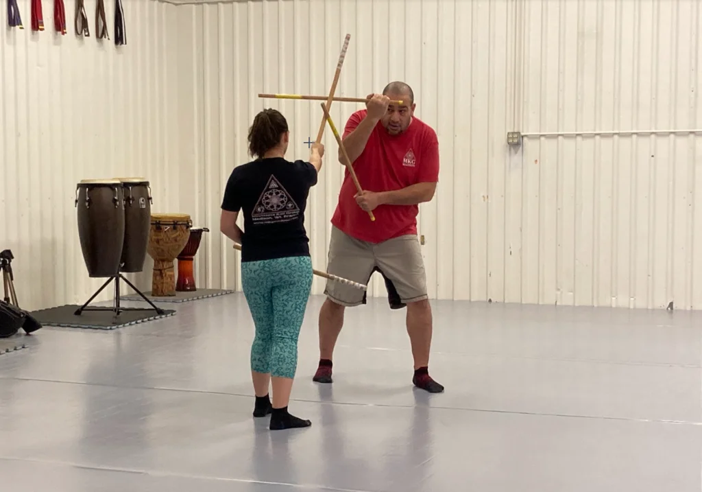 An instructor demonstrating Filipino martial arts stick fighting techniques with a student